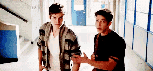 two young men are standing in a hallway next to each other .