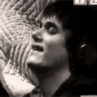 a man is wearing headphones and singing into a microphone in a black and white photo .
