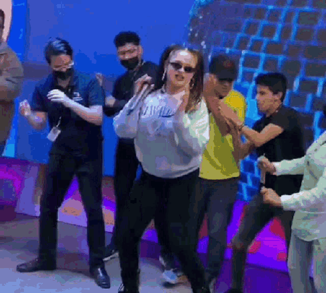 a group of people are dancing in a room with a woman wearing sunglasses and a sweatshirt that says " wild "