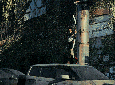 a woman is standing on top of a car in front of a building that says adidas