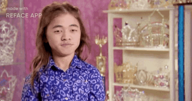 a young girl wearing a blue shirt is standing in front of a shelf full of crowns .
