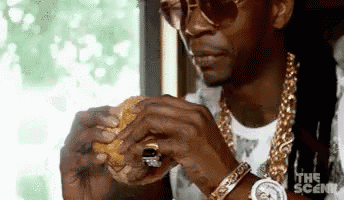 a man wearing sunglasses is eating a hamburger .