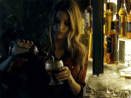 a woman in a red shirt is pouring a drink from a shaker into a wine glass