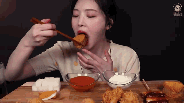 a woman is eating fried food with chopsticks and sauces