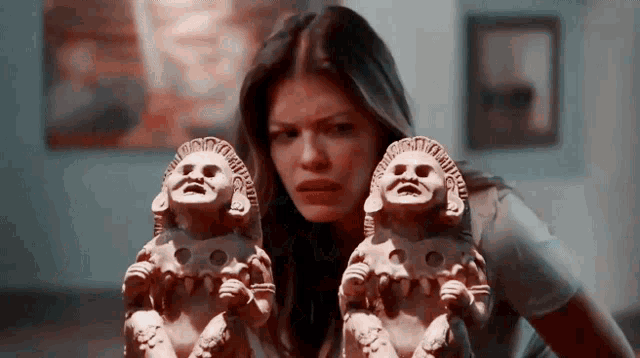 a woman is holding two statues of a baby with a face on them