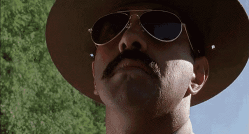a man wearing a hat and sunglasses looks up at the camera