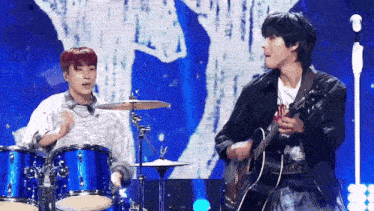 a man playing drums and a man playing a guitar on a stage .