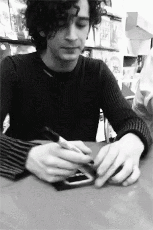 a man with curly hair is sitting at a table writing on a piece of paper