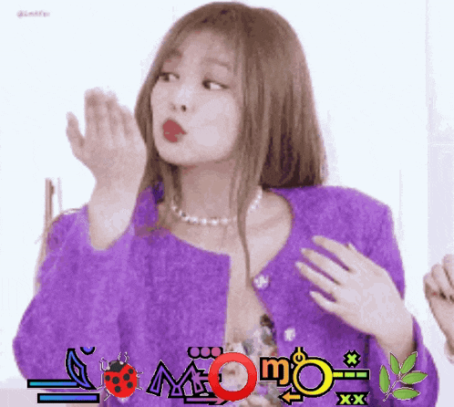 a woman wearing a purple jacket and a ladybug necklace is blowing a kiss