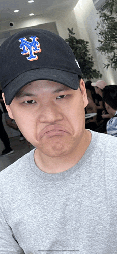 a man wearing a new york mets hat makes a face