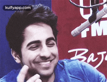 a man is smiling in front of a microphone while wearing a blue shirt