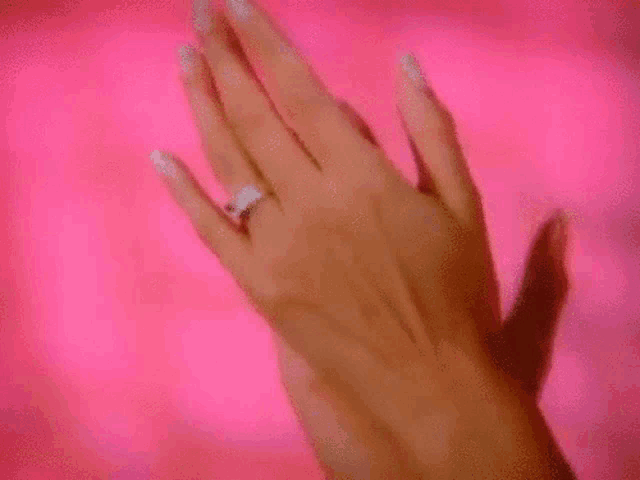 a close up of a woman 's hand wearing a diamond ring on a pink background .