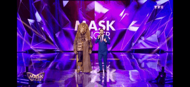 a man in a suit stands on a stage in front of a mask singer sign .