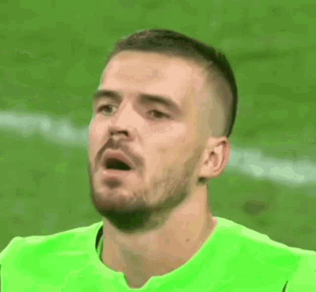 a soccer player wearing a green jersey is making a funny face on the field .