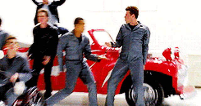 a group of men in overalls are standing in front of a red car