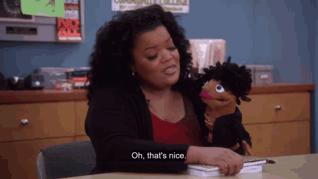 a woman sitting at a desk with a puppet and says oh that 's nice