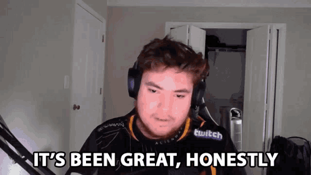 a man wearing headphones and a twitch shirt says it 's been great honestly