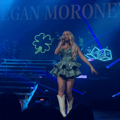 a woman in a green dress stands on stage with her arms in the air in front of a sign that says megan moron