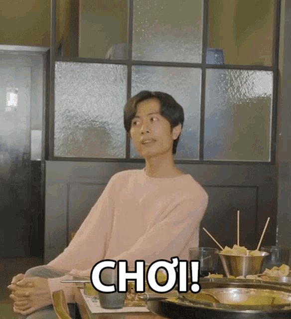a man in a pink sweater sits at a table with a sign that says choi on it