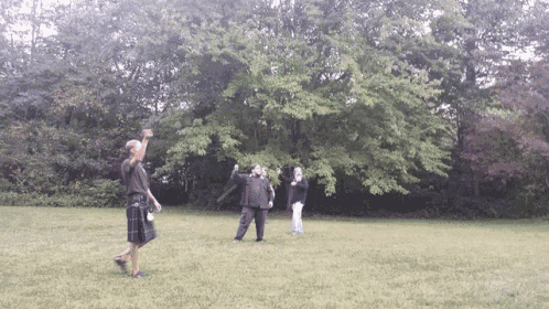 a man in a kilt stands in a grassy field with other people