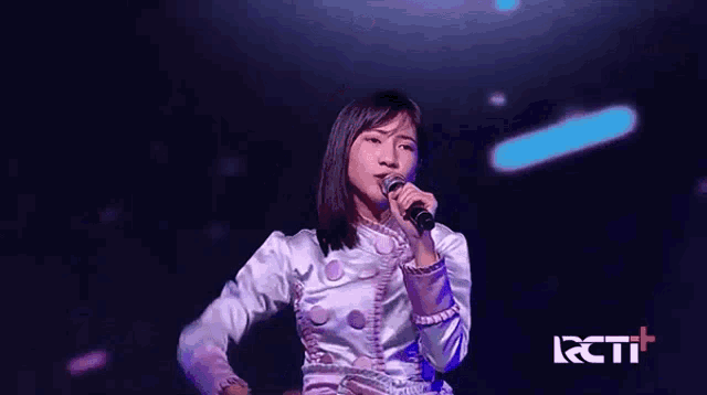 a woman is singing into a microphone on a stage in front of a rcti logo .