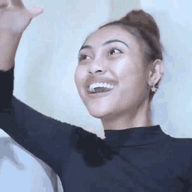 a woman wearing a black shirt and earrings is smiling and waving her hand