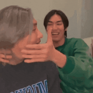 a man covering another man 's mouth while wearing a michigan shirt