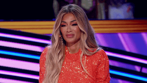 a woman in a red sequined dress is sitting on a stage with a purple background .