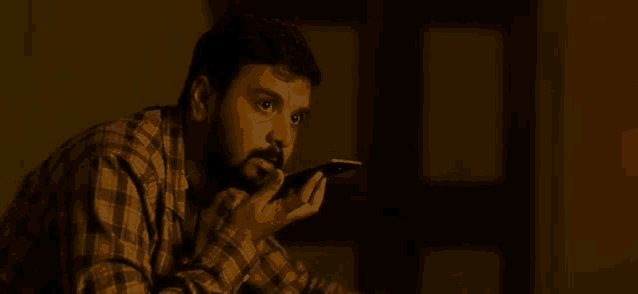 a man with a beard is holding a cell phone to his mouth in a dark room .