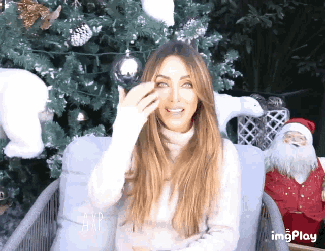 a woman is sitting in front of a christmas tree holding a christmas ornament in her hand