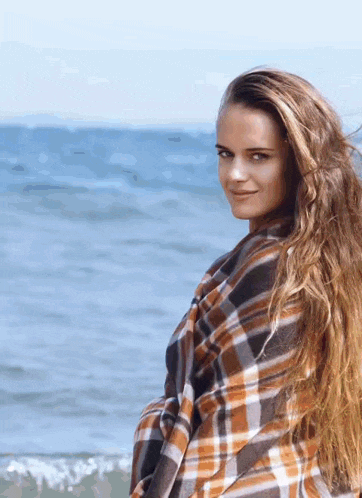 a woman with long hair is wrapped in a plaid blanket on the beach .