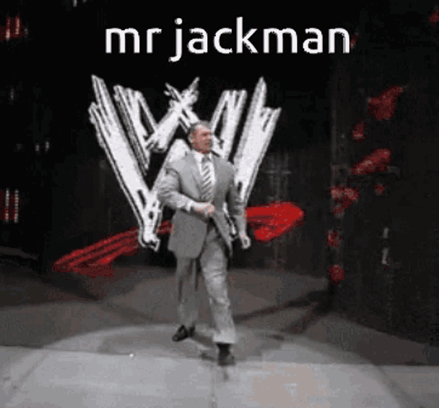 a man in a suit and tie is walking on a stage in front of a wrestling logo .