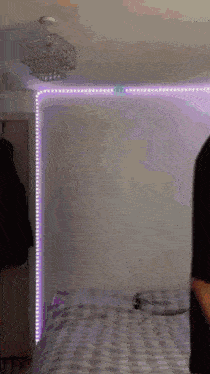 a person is standing next to a bed in a bedroom with a chandelier hanging from the ceiling .
