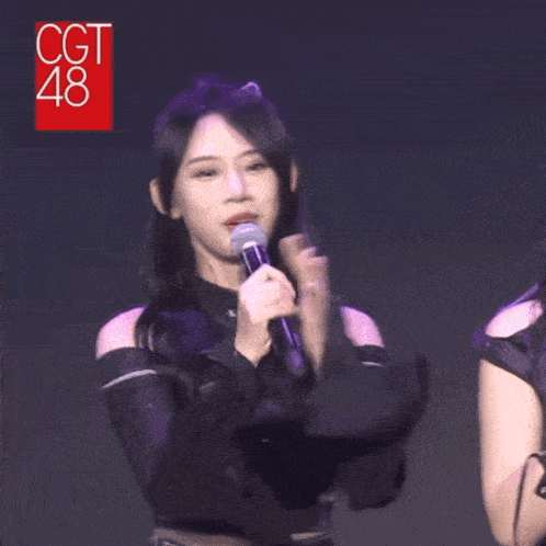 a woman with long black hair is holding a microphone in her hand