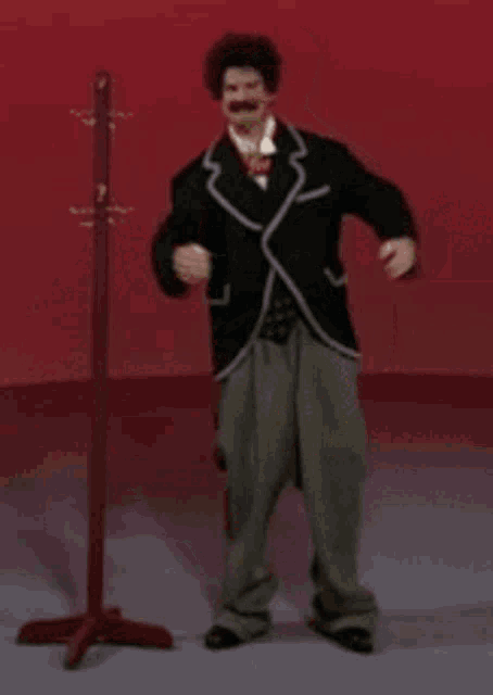 a man in a suit and yellow shorts is standing next to a wooden coat rack