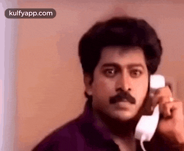 a man with a mustache is talking on a cell phone and making a funny face .