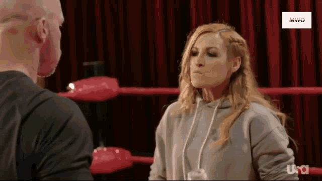 a man and a woman are standing in a wrestling ring and the woman is wearing a hoodie .