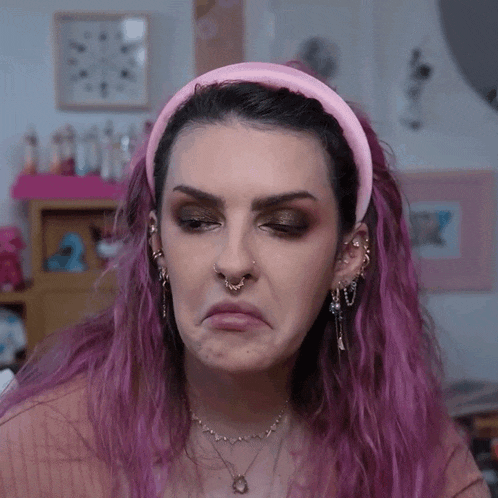a woman with purple hair and a pink headband making a face