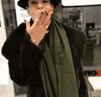 a woman wearing a fur coat and a green scarf is blowing a kiss