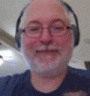 a man with a beard and glasses is wearing headphones and a blue shirt .