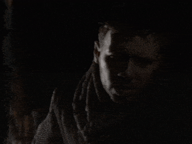 a man with a scarf around his neck is standing in the dark .