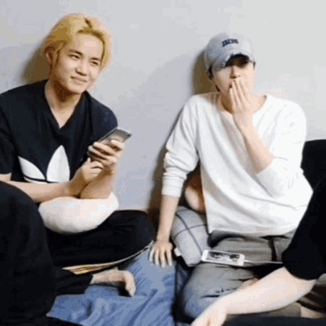 a group of young men are sitting on a couch looking at their cell phones .