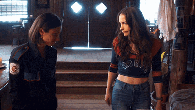 two women are standing next to each other and one of them is wearing a crop top that says ' nor ' on it