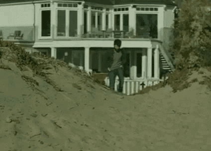 a man is walking down a sandy hill in front of a house .