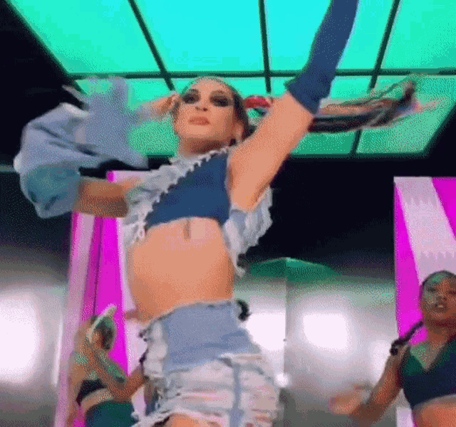 a woman in a crop top and shorts is dancing on a stage with other women .