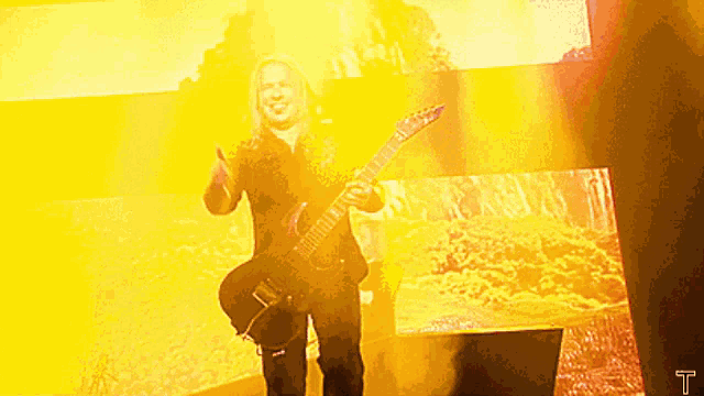 a man is playing a guitar in front of a yellow background with the letter t on it
