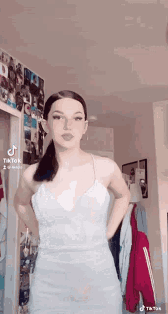 a woman in a white dress is standing in front of a wall with pictures on it .