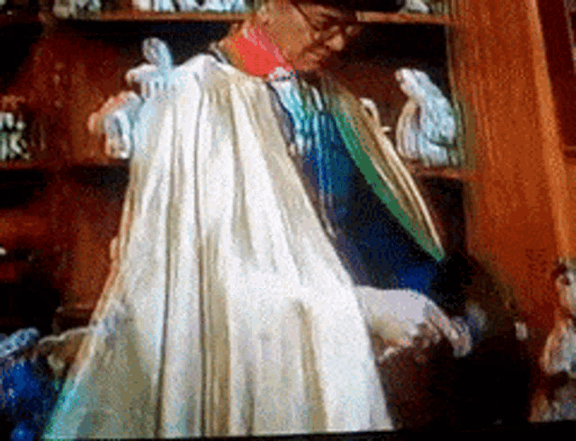 a man wearing a white cape is standing in front of a shelf full of figurines