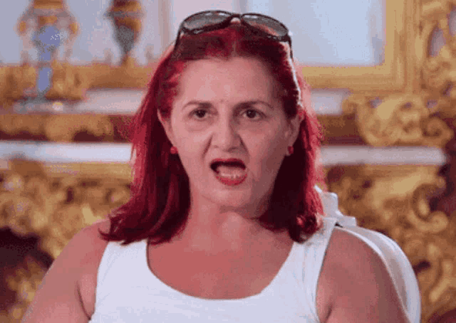 a woman with red hair wearing sunglasses and a white tank top is making a funny face