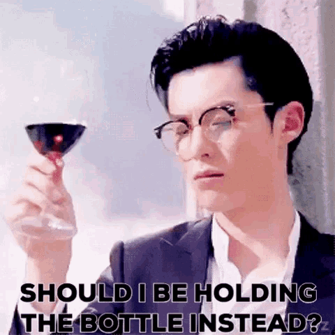 a man in a suit and glasses is holding a glass of wine and asking should i be holding the bottle instead ?